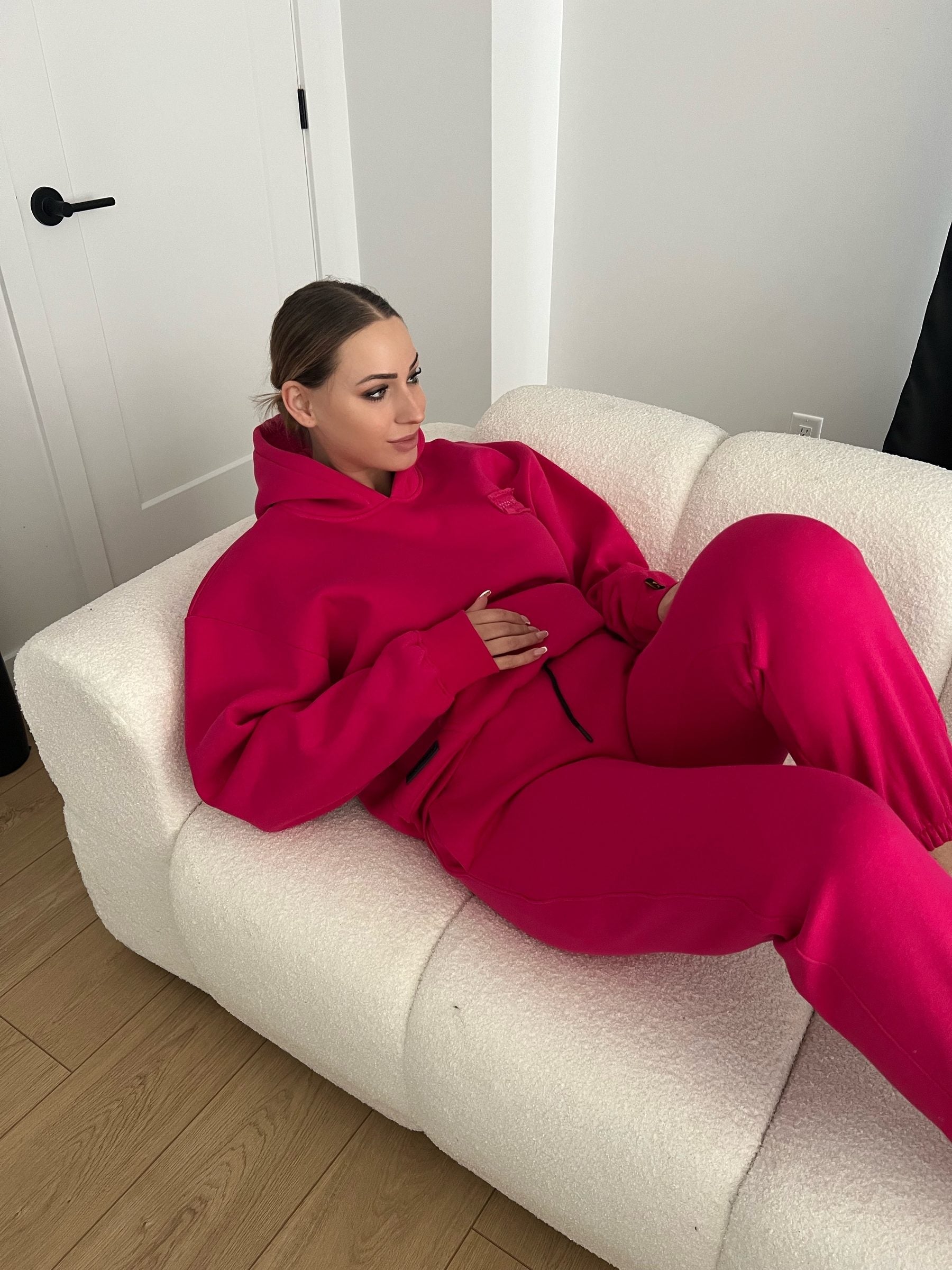 Woman lounging on a sofa in the Dope Beyond Hot Pink hoodie and joggers set