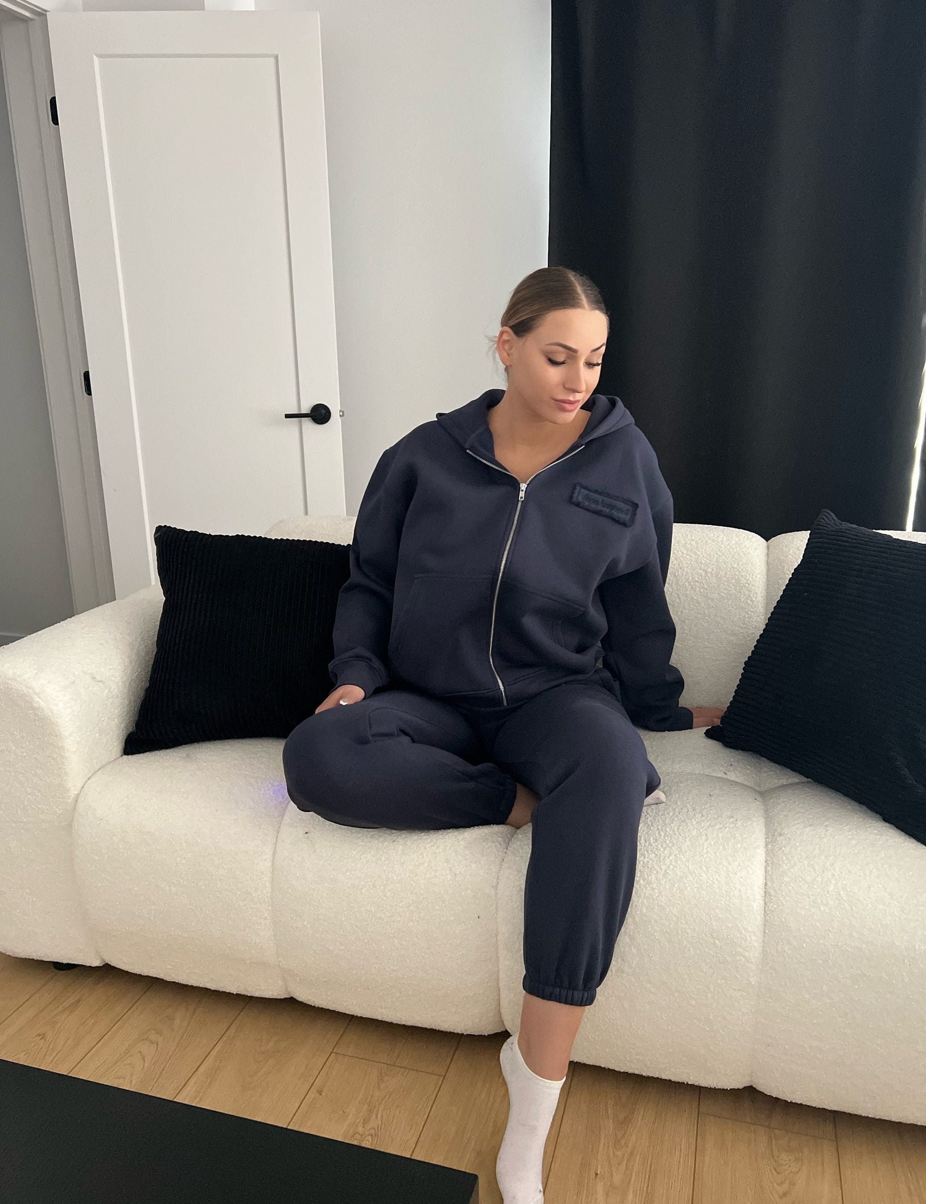 Woman sitting forward on a sofa in the Dope Beyond Ink Navy zip hoodie and joggers set