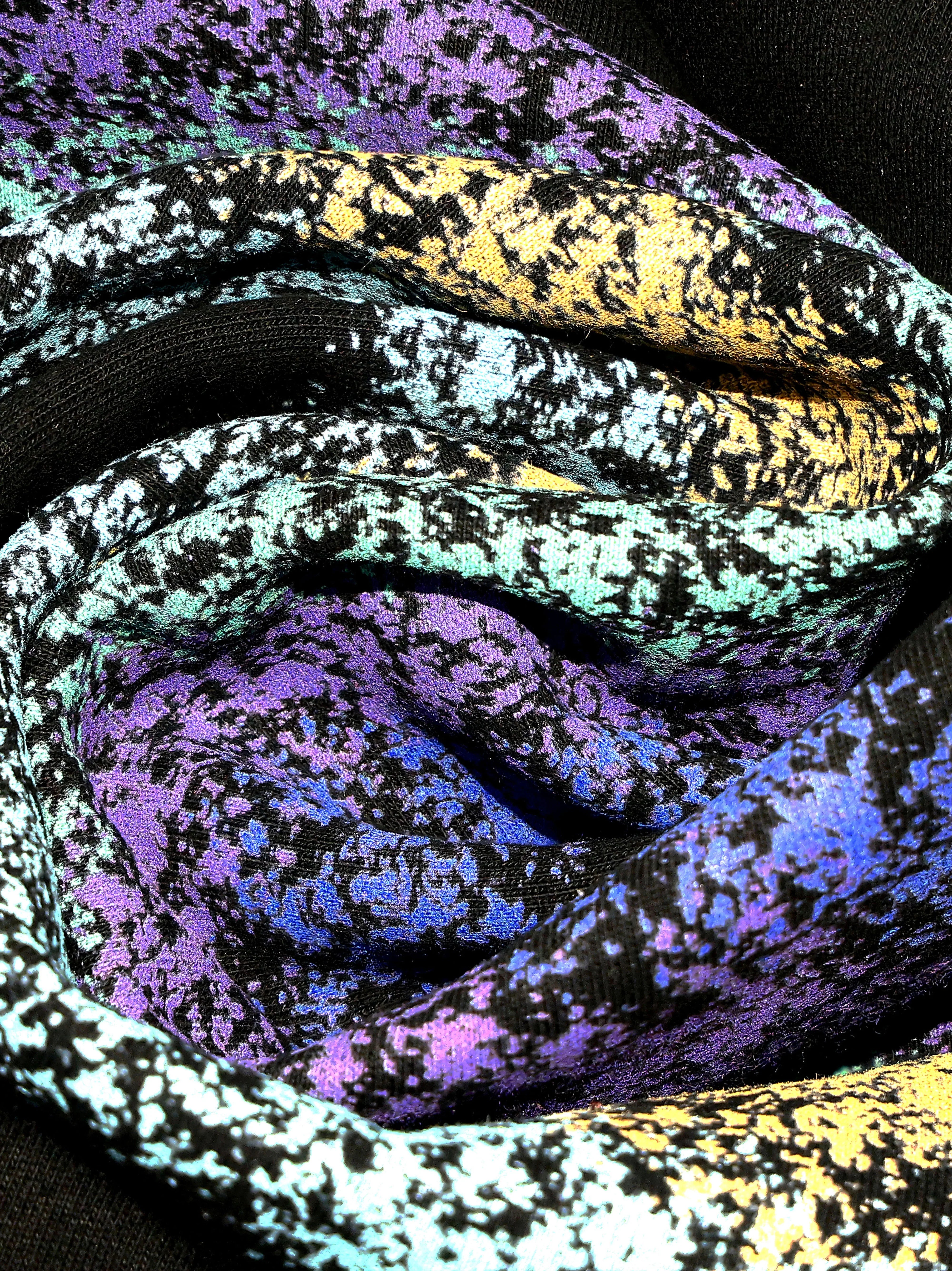 Close-up of multicolored abstract streetwear fabric, featuring vibrant purple, blue, yellow, and black patterns.