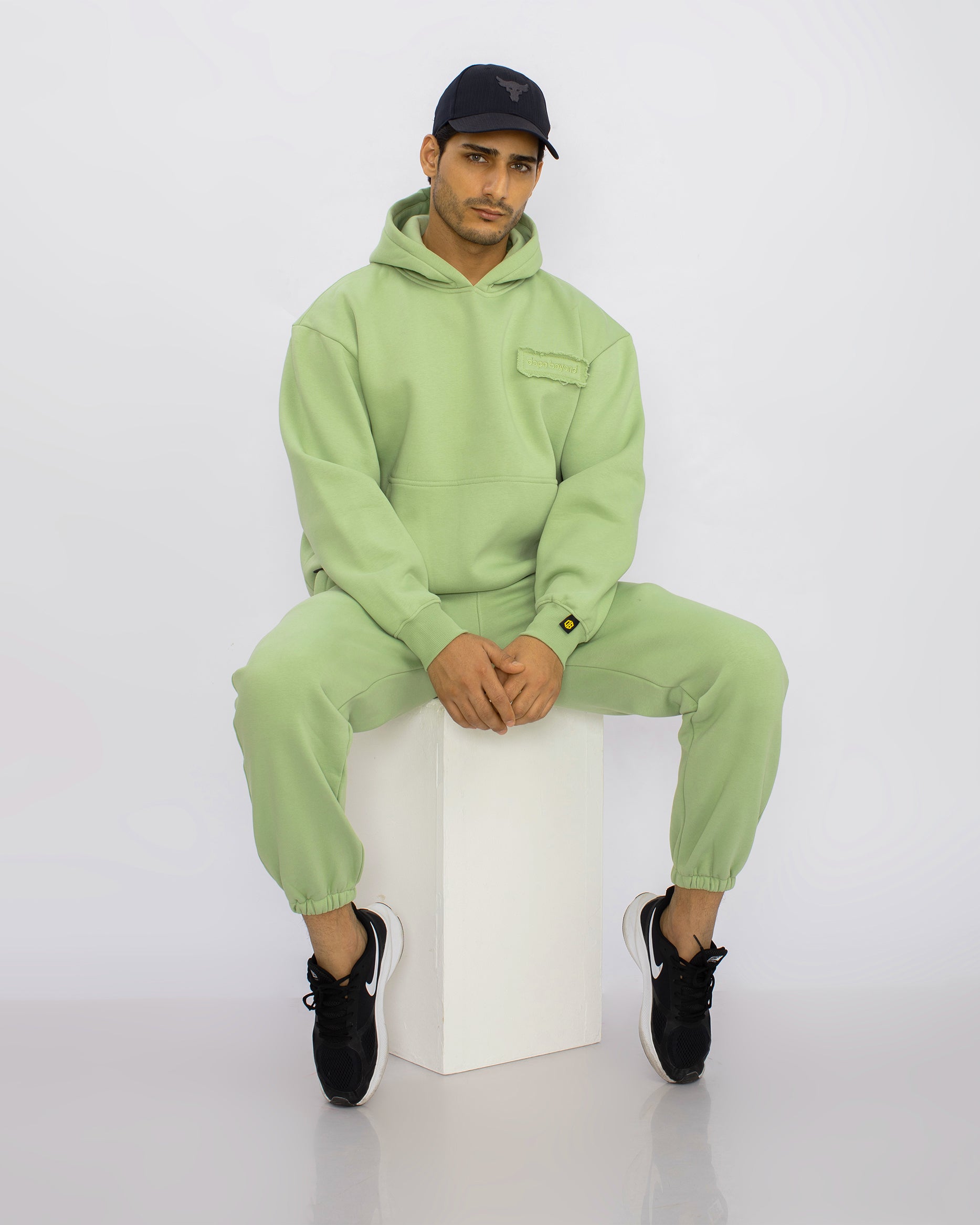 Man wearing light green dopebeyond hoodie and joggers, black cap and sneakers, streetwear style