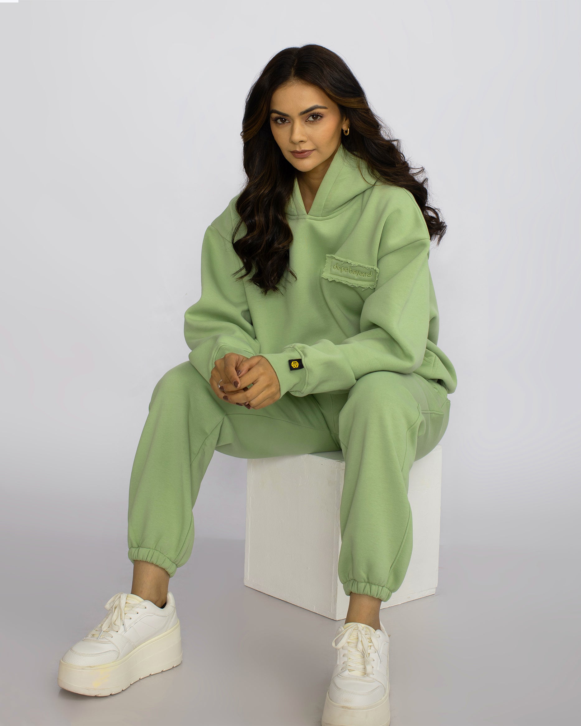 Woman modeling light green dopebeyond streetwear hoodie and joggers, white sneakers, studio setting
