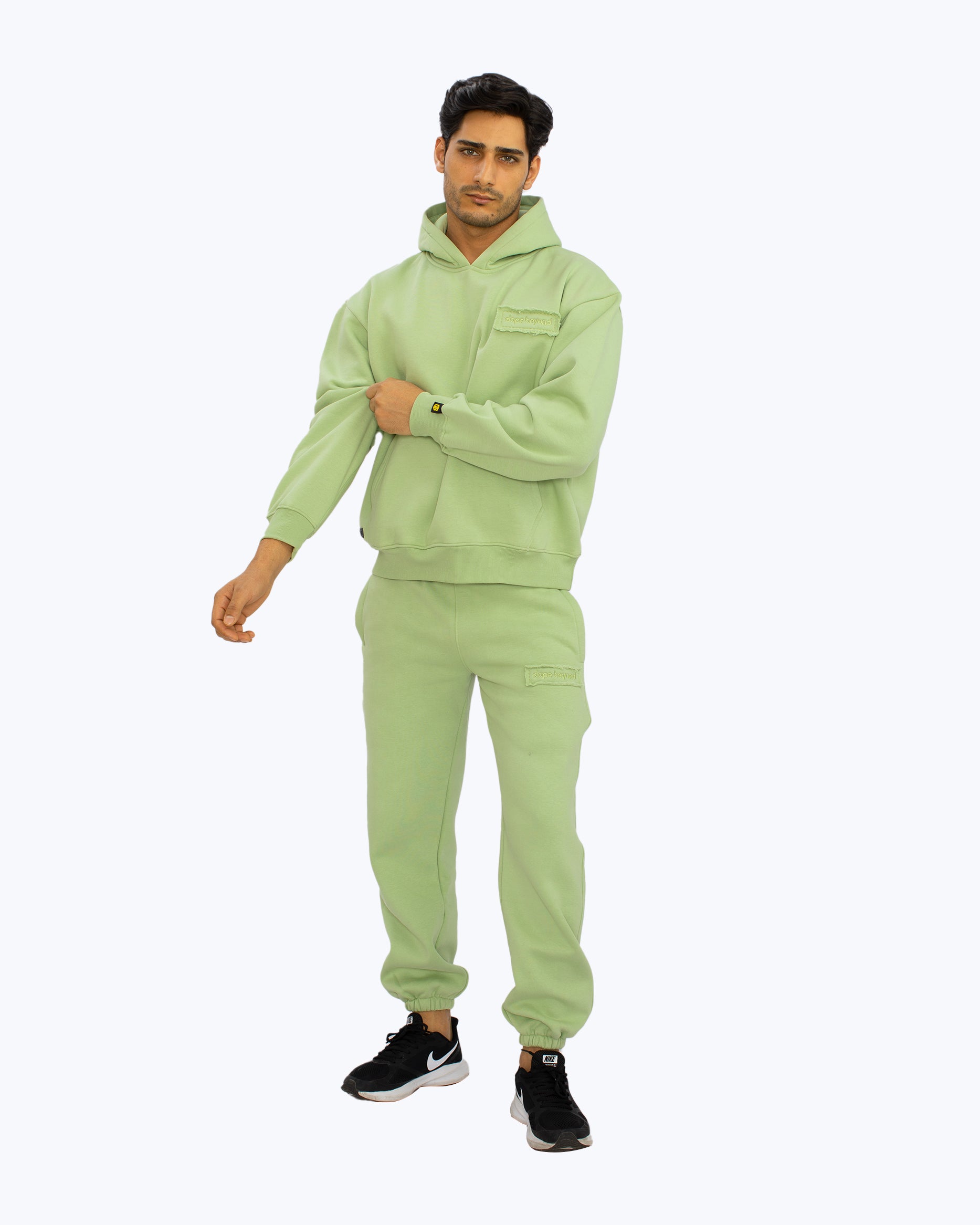 Man wearing light green Dope Beyond streetwear hoodie and joggers set on white background