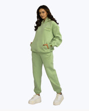 Woman in sage green dopebeyond streetwear hoodie and joggers set on white background