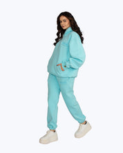 Woman modeling aqua blue Dope Beyond streetwear tracksuit with logo, white sneakers, studio shot