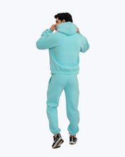 Man in turquoise streetwear hoodie and joggers from dopebeyond, rear view on white background
