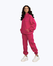 Woman in bright pink Dope Beyond streetwear tracksuit with white sneakers, posing on white background.