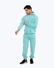 Man wearing light blue dopebeyond hoodie and joggers streetwear set against white background