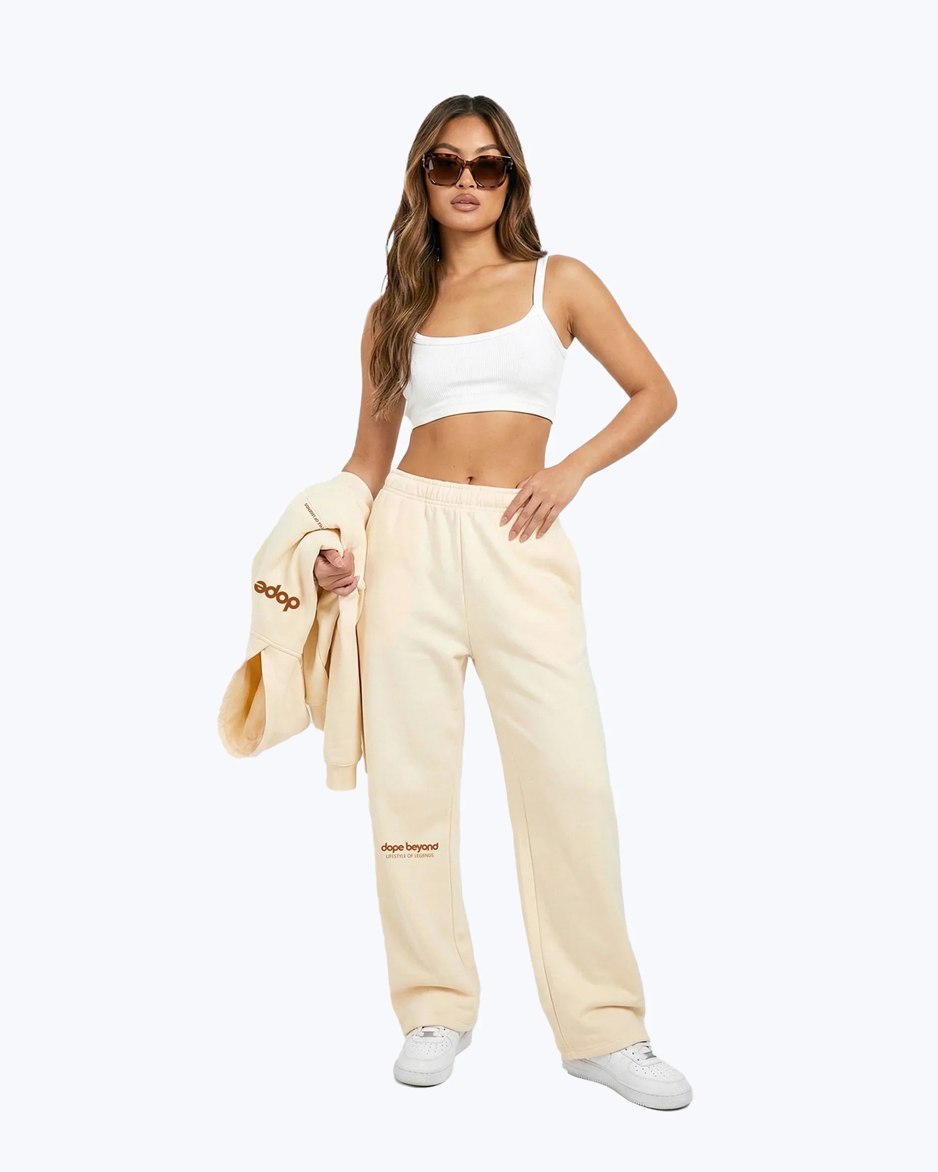 Woman wearing beige Dope Beyond heavyweight joggers and white crop top, holding matching hoodie