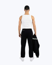 Man in dopebeyond black gym joggers and white tank, holding hoodie with 'beyond' logo