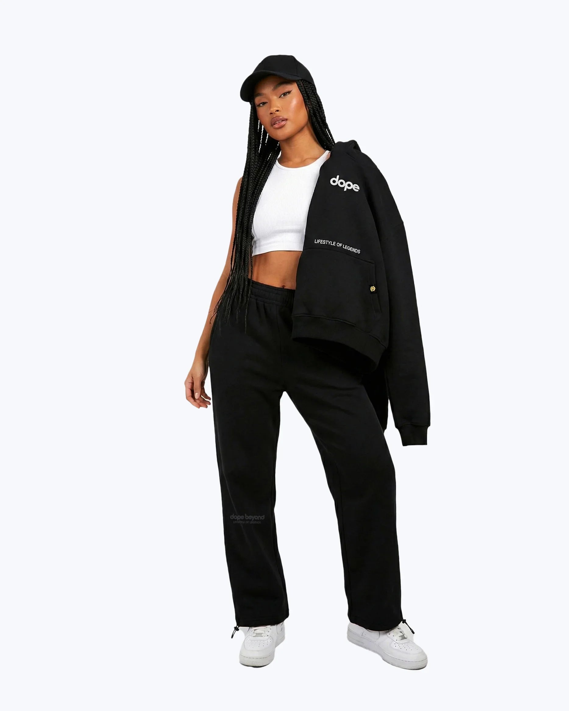 Woman in Dope Beyond black streetwear joggers, hoodie, and cap, white crop top