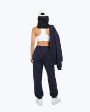 Woman wearing Dope Beyond navy heavyweight joggers, white crop top, and cap, back view