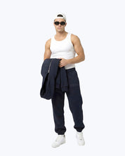 Man wearing Dope Beyond Ink navy heavyweight joggers, white tank top, cap, and sunglasses.