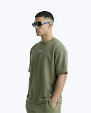 Model in olive green Dope Beyond™ streetwear t-shirt and sunglasses against white background