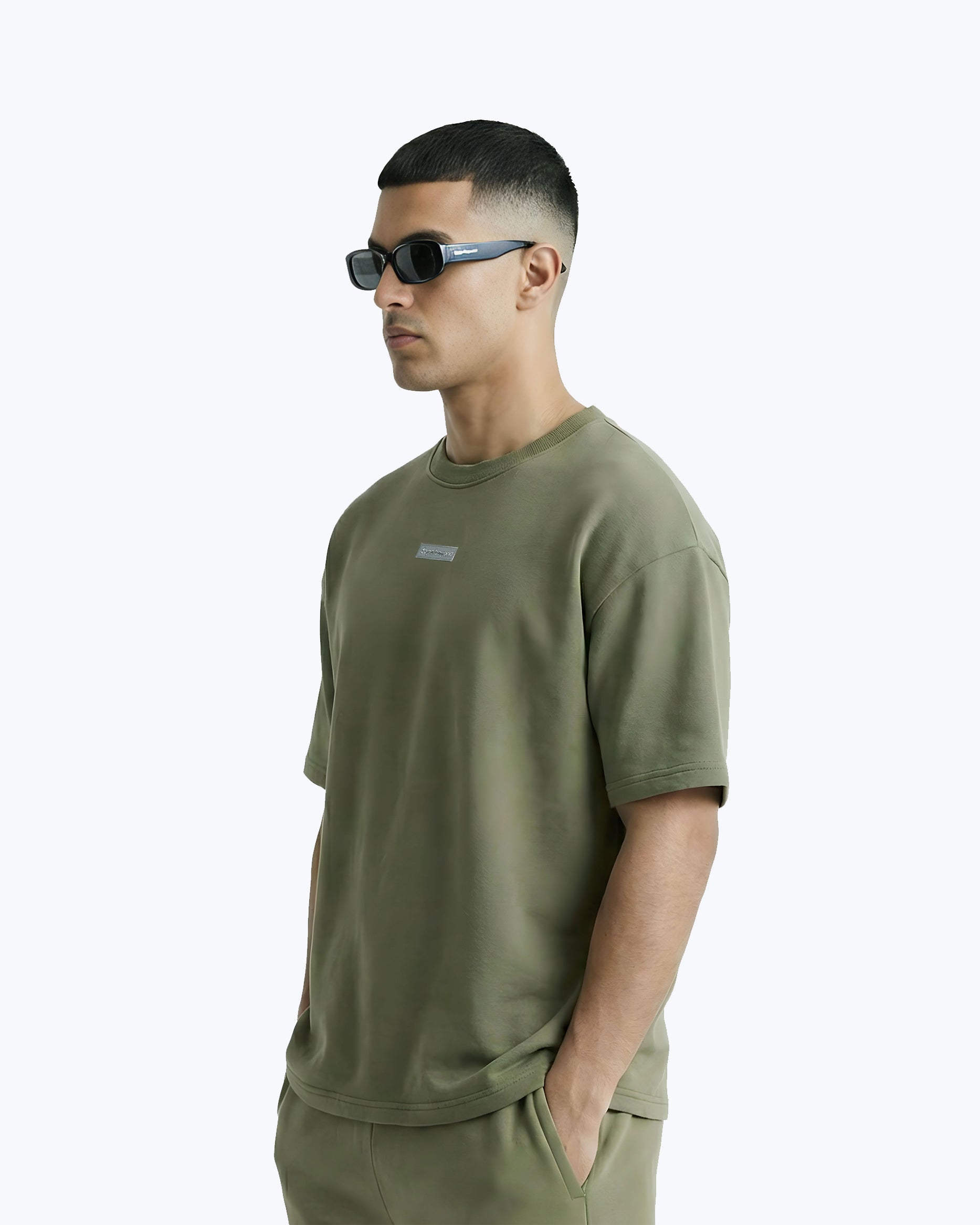 Model in olive green Dope Beyond™ streetwear t-shirt and sunglasses against white background