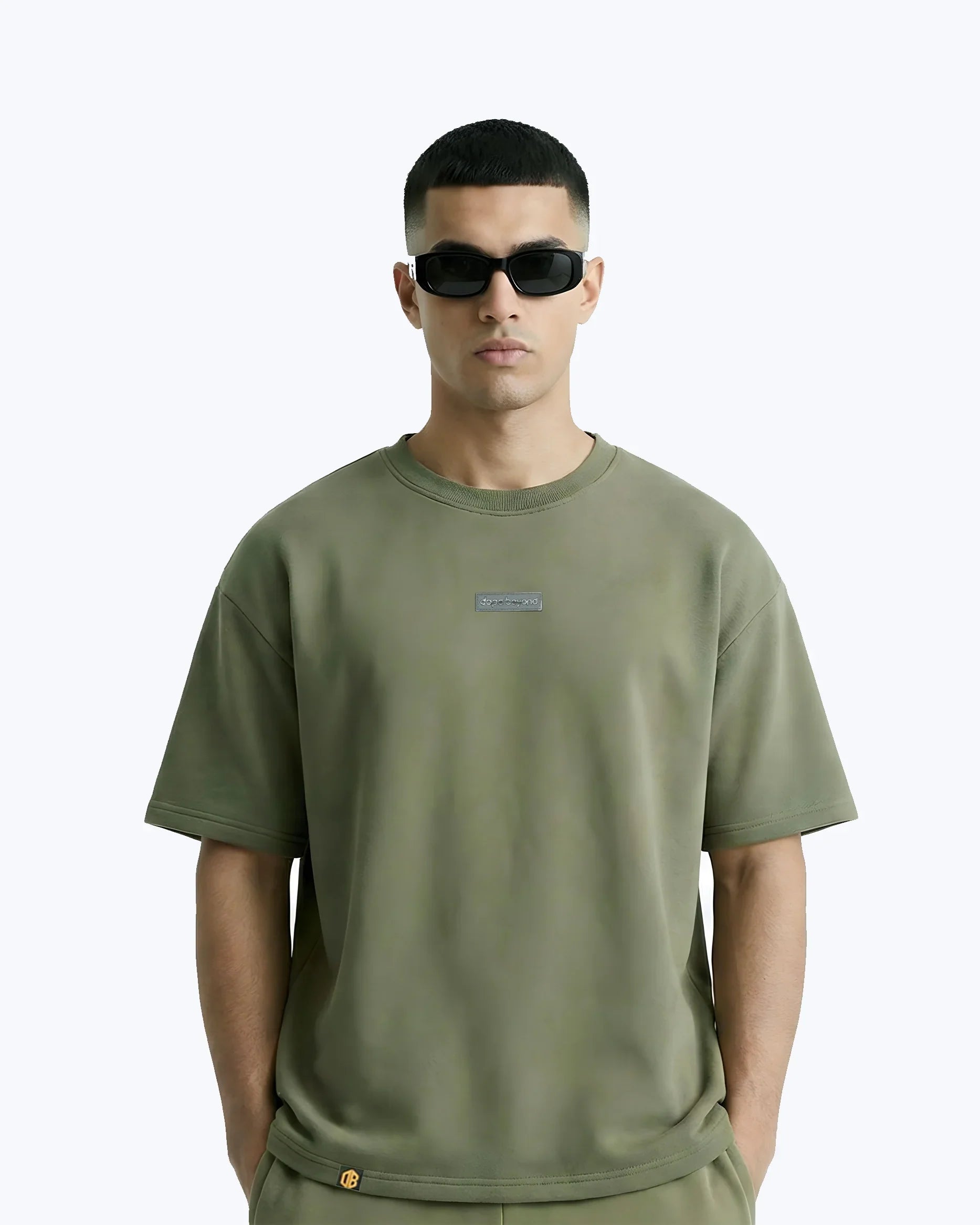Model wearing olive green Dope Beyond streetwear t-shirt and sunglasses, minimal background