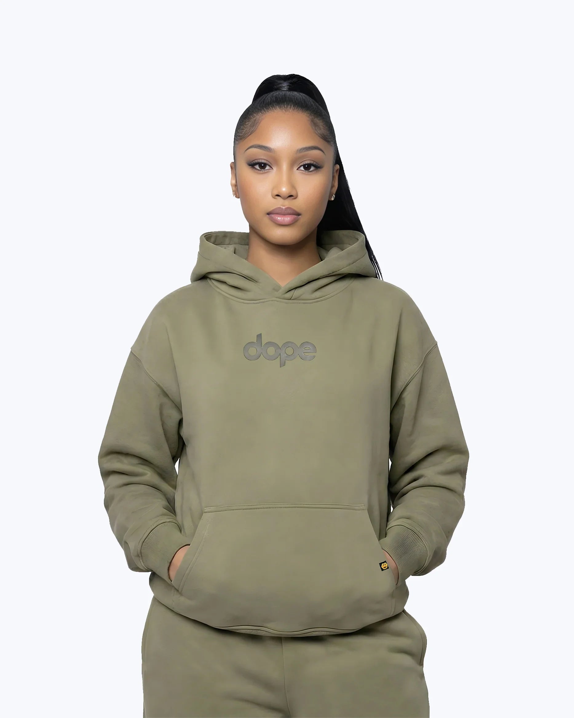 Woman wearing olive green Dope Beyond streetwear hoodie with front logo, hands in pocket