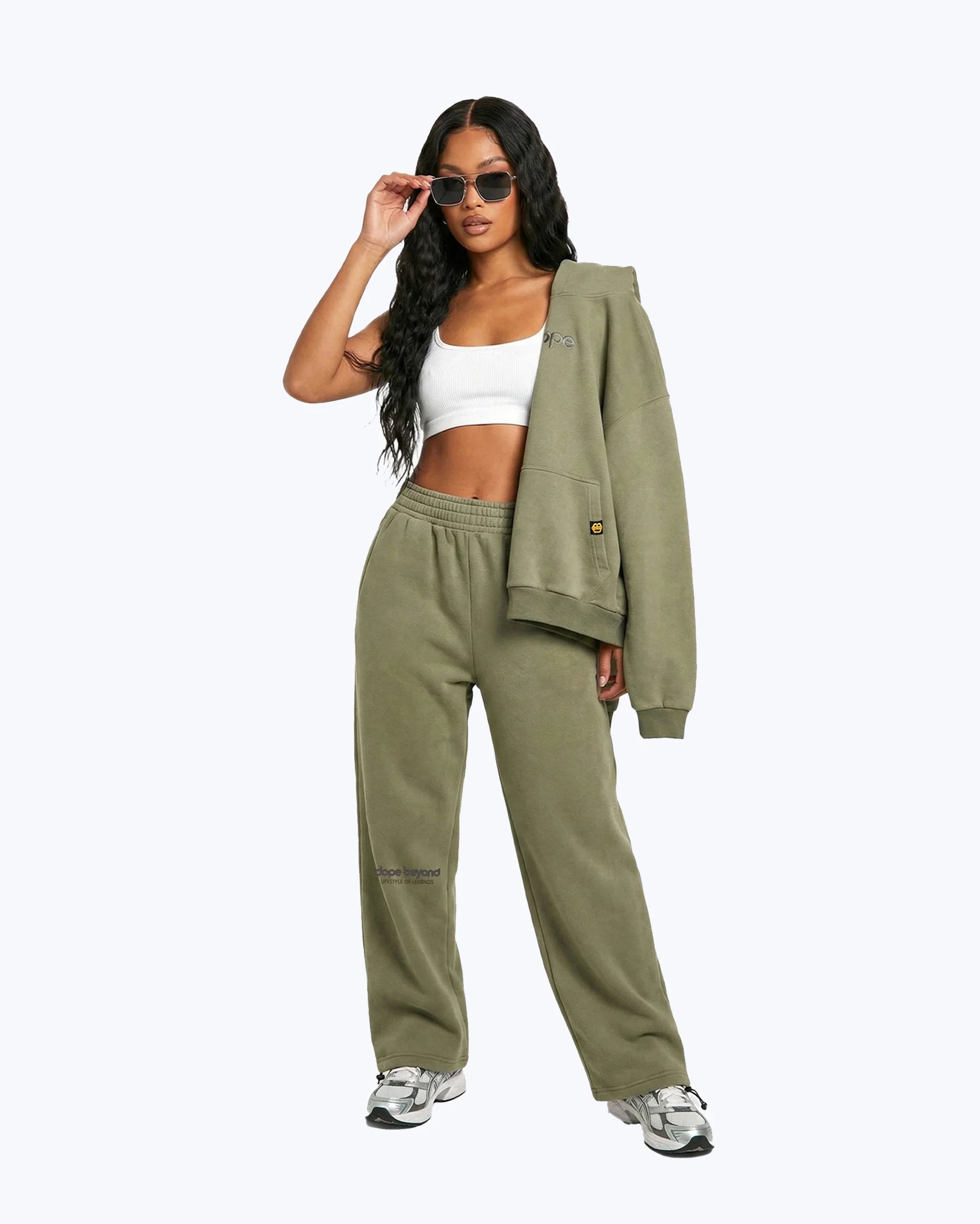Woman wearing dopebeyond olive green jogger set, white crop top, sunglasses, and sneakers