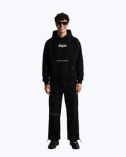Man in black Dope Beyond streetwear cordset, hoodie and pants, standing and smiling