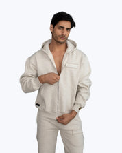 Man wearing light beige dopebeyond hoodie and sweatpants, streetwear style, studio background
