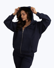 Woman wearing navy blue dopebeyond streetwear zip hoodie and sweatpants, white background