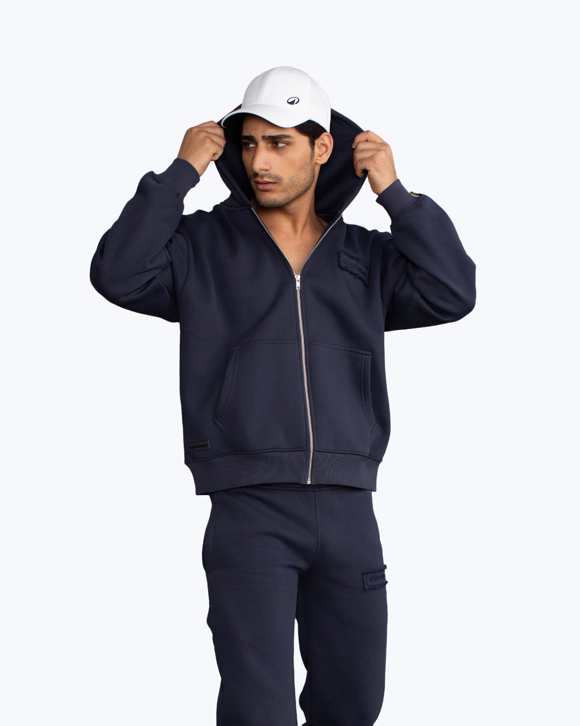 Man in navy DopeBeyond streetwear zip hoodie and joggers, white cap, urban apparel