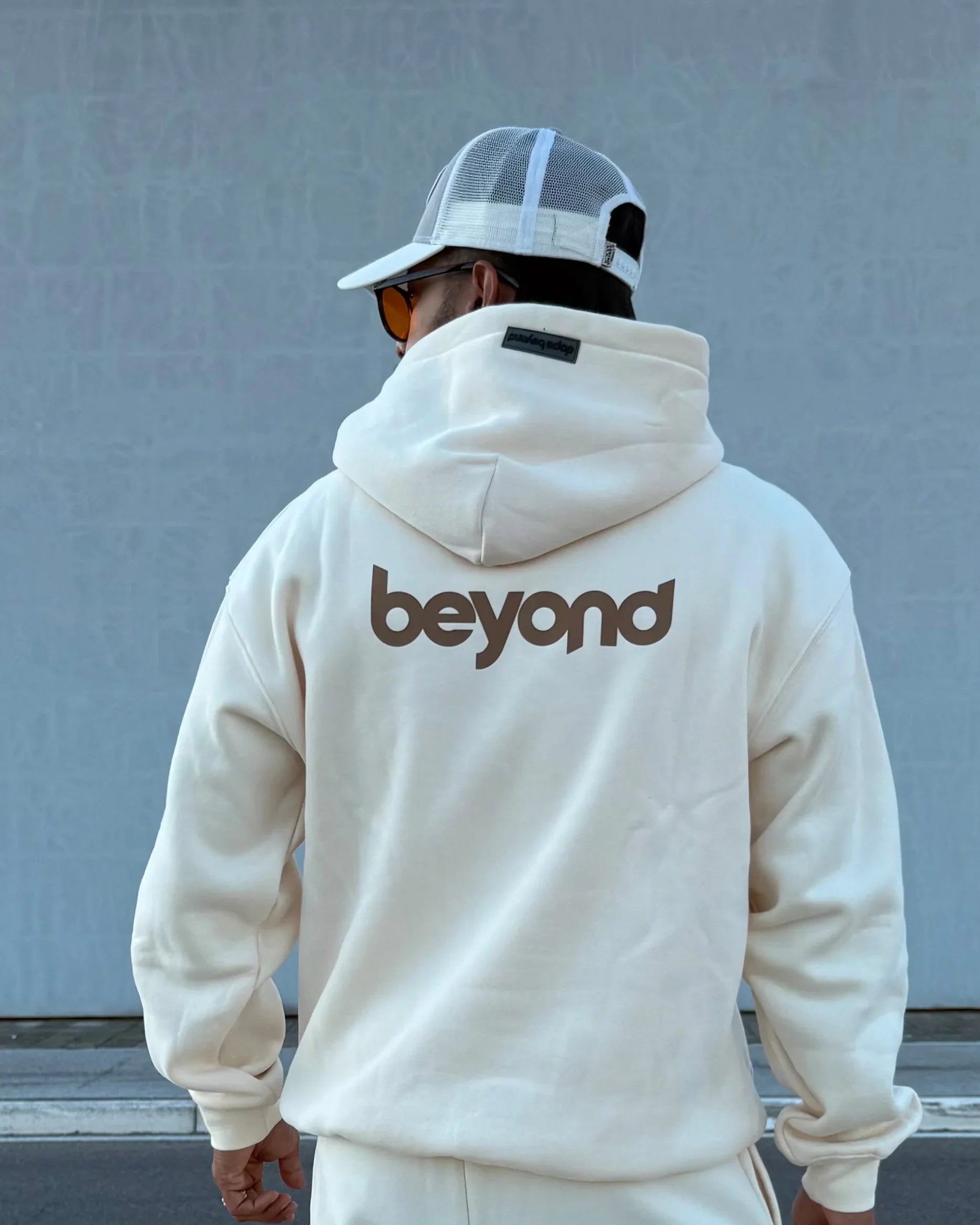 Man in cream hoodie with 'beyond' print, streetwear style, dopebeyond clothing brand