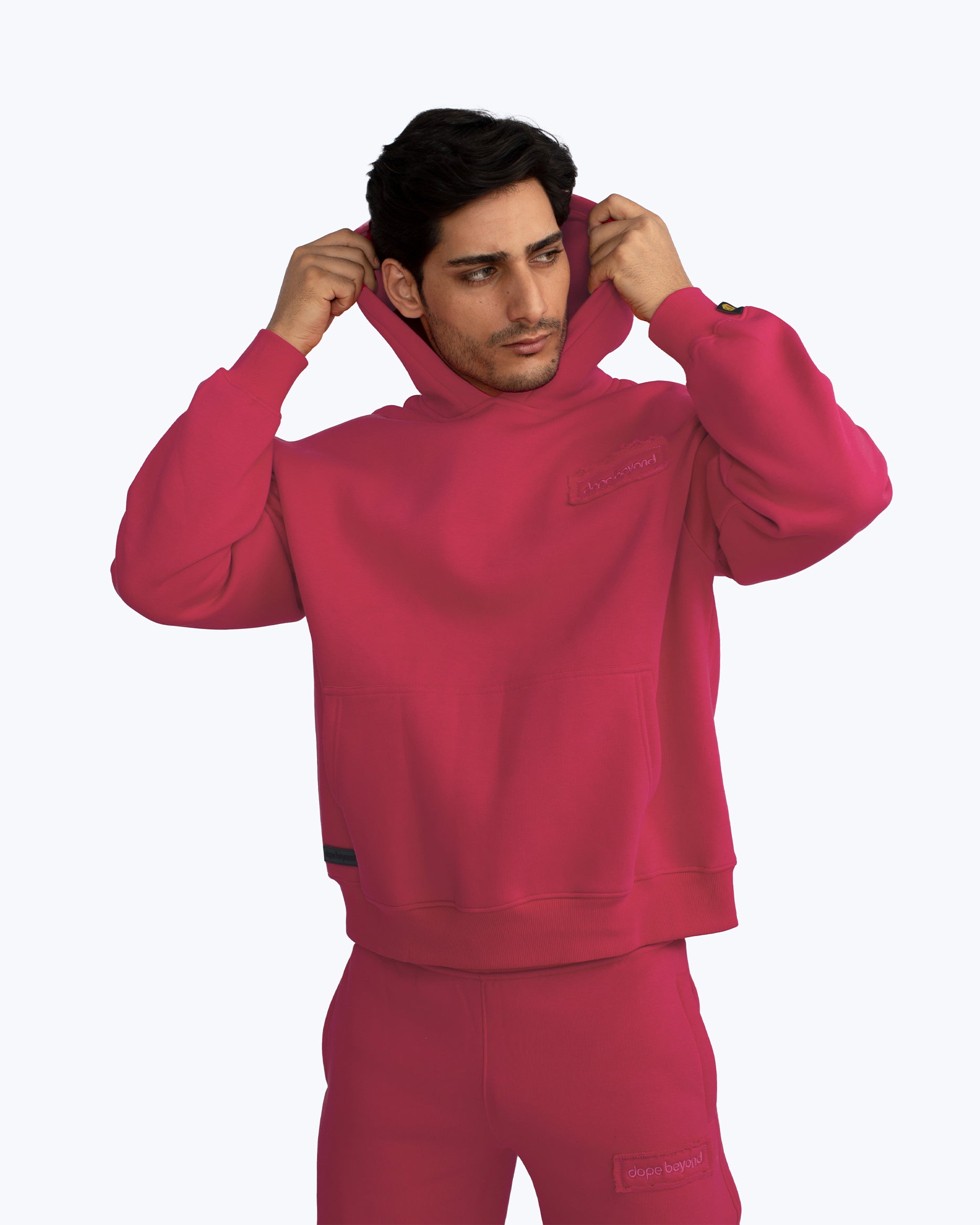 Man wearing vibrant pink Dope Beyond streetwear hoodie and joggers, adjusting hood