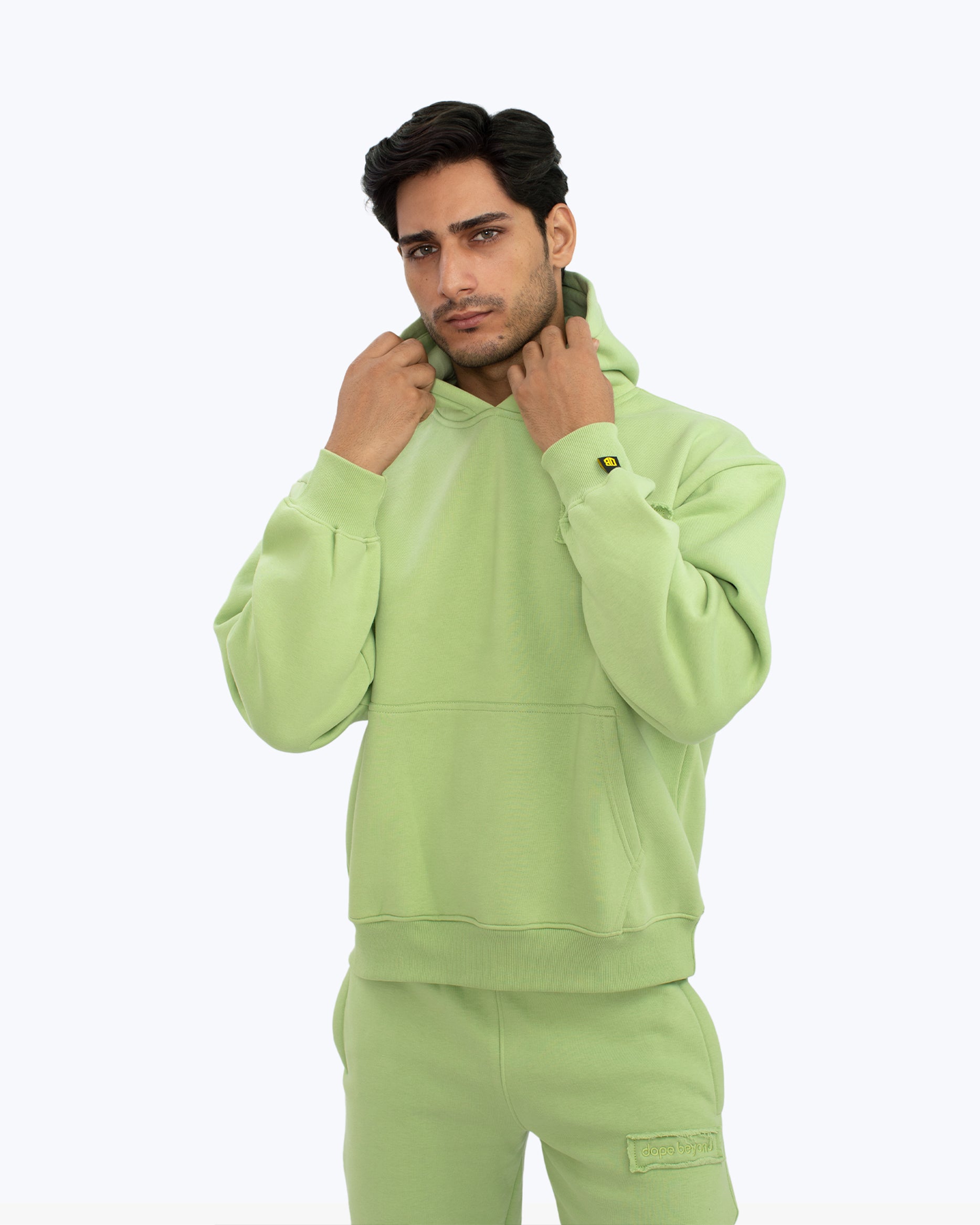 Man wearing light green dopebeyond streetwear hoodie and joggers, minimalist background