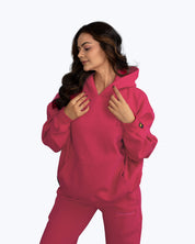 Woman wearing a bold pink dopebeyond streetwear hoodie and joggers set on light background