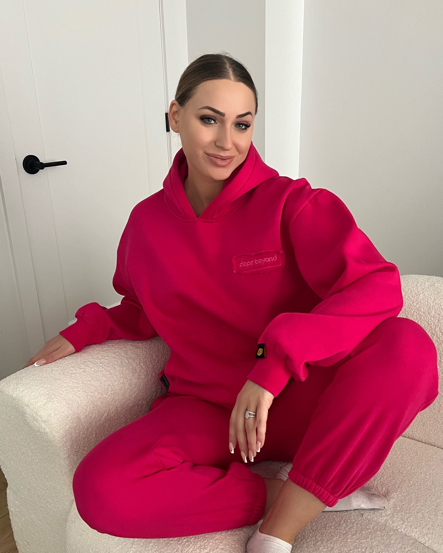 Woman in hot pink dopebeyond hoodie and joggers relaxing on a white chair, streetwear style