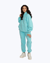 Woman in aqua blue streetwear jogger set from dopebeyond with white sneakers on plain background