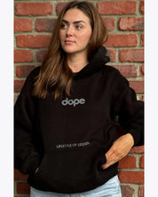 Woman in black dopebeyond hoodie with 'dope' and 'lifestyle of legends' text, brick wall background