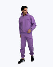 Man wearing purple dopebeyond streetwear hoodie and joggers, black sneakers, on light background