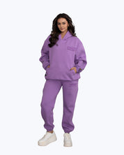 Woman modeling purple dopebeyond streetwear hoodie and jogger set with logo patch.