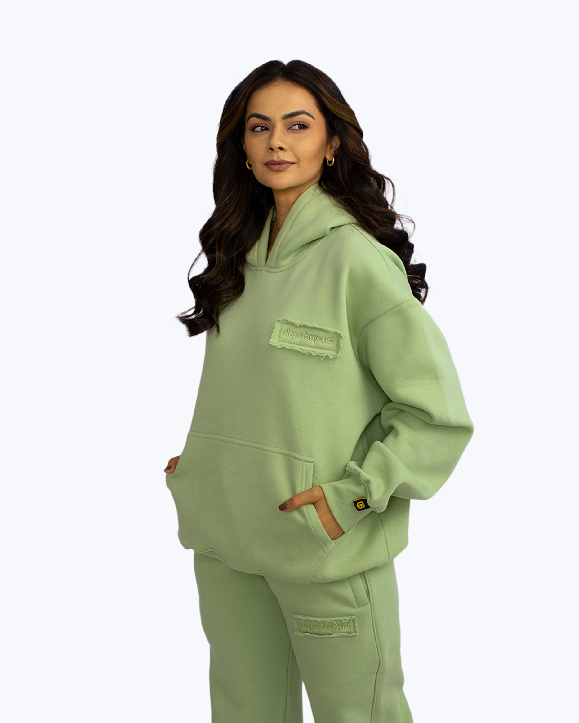 Woman in mint green dopebeyond streetwear hoodie and joggers, hands in pocket, studio background