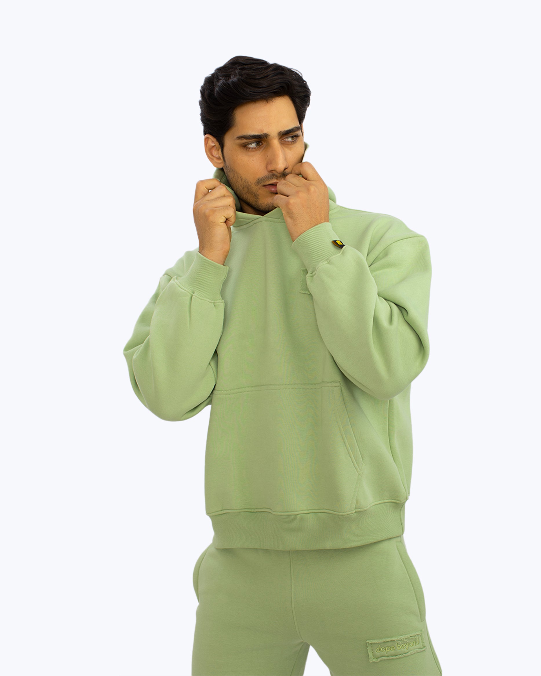 Man in mint green streetwear hoodie and sweatpants by dopebeyond against light background